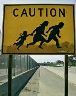 Znak drogowy ostrzegający przed przebiegającymi przez autostradę imigrantami 
