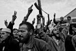 Wydarzenia – fotoreportaż  MIEJSCE 2. Libia 2011. W powtarzanym przez stacje telewizyjne przemówieniu Kaddafi mówił, że jeśli naród go nie kocha, to sam zasłużył sobie na śmierć. Przez kilkadziesiąt lat rodziny ofiar dyktatury Kaddafiego musiały milczeć. Po wybuchu rewolucji w Bengazi rozpoczęło się rozliczanie przeszłości. Trzymana na ramionach 13-latka wykrzykuje do megafonu hasła przeciw dyktatorowi. Obok znajduje się zdjęcie jej zamordowanego ojca. Uroczyste pogrzeby zdarzały się na placu dość często. Libijczycy walczyli tym, co mieli: trafiały się  i radzieckie granaty rozpryskowe, i zardzewiałe karabiny maszynowe. Wiele miejsc wyglądało jak pobojowisko. Wśród żelastwa znaleźć można było m.in. stare głośniki, przez które niedawno słuchano przemówień dyktatora.  Do kostnicy na obrzeżach miasta wciąż przywożono nowe zwłoki. Były wśród nich osmalone ciała żołnierzy, którzy odmówili wykonania rozkazu strzelania do cywilów. Zostali zamordowani przez swoich przywódców, a po śmierci – podpaleni.  Tego, oczywiście, nie fotografowałem,  bo widok był przerażający. 