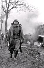 Niemiecki żołnierz mijający płonącą amerykańską półgąsienicę. Ardeny, 17 grudnia 1944 r. 