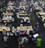 Refugees sit at tables installed in an exhibition hall of the Munich fairground upon arrival in the Bavarian city, southern Germany, on September 7, 2015. The numbers of migrants have spiked since September 4, 2015, when Austria and Germany threw open their borders and eased travel restrictions to allow in thousands who had made it to Hungary, which has balked at the influx. AFP PHOTO / CHRISTOF STACHE