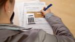 Woman hand filling income tax forms with calculator