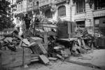 Fotoreporter. Wielokrotnie fotografował w strefach konfliktów zbrojnych oraz konsekwencje wojen m.in. w Ukrainie, Iraku, Afganistanie Pierwsza refleksja? Jaka piękna architektura Warszawy w tle. Jaka szkoda, że jej już nie ma. Druga refleksja dotyczy tego, jak bardzo amatorsko zbudowane są barykady – z resztek mebli, gruzu. Na szczycie dwóch ludzi, cywilnie ubranych – prowizoryczny opór. To jest zdjęcie o utracie – tego miasta już nie ma. To, co mnie w tym zdjęciu zastanawia, to miejsce, z którego sfotografowano scenę. Autor jest po niewłaściwej stronie barykady, stoi od strony atakujących, czyli Niemców. Pewnie to zdjęcie zostało wykonane w momencie ciszy, zawieszenia w walkach. Mimo to wyjście na drugą stronę musiało się wiązać z dużą odwagą. Osią tego zdjęcia jest jednak barykada, pejzaż miejski, to nie jest zdjęcie akcji. Gdy fotografujesz wojnę, czasem wydarzenia dzeją się w miejscu, w którym jesteś. Najlepiej dla dokumentowania i raportowania tego, co się dzieje, gdy fotograf ma czas i może zrobić wiele kadrów, podejść bliżej do bohaterów, ale też odejść, by pokazać kontekst czy skalę. Ale najczęściej, gdy fotografujesz wojnę, tej możliwości nie ma. Nie działa się według planu, a raczej na ile możliwości daje sytuacja. Śródmieście Północne, 5 sierpnia 1944 roku. Barykada przy ulicy Moniuszki 2a przy wylocie placu Napoleona. Zdjęcie wykonane przez Joachima Joachimczyka „Joachima”.