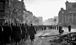 Polskie wojsko przechodzi przez plac Trzech Krzyży. Po wojnie podawano, że był to przemarsz na defiladę w Al. Jerozolimskich 19 stycznia. Istniały wątpliwości co do datowania fotografii, ponieważ nie widać śniegu, jaki zalegał wówczas na ulicach  