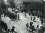 Uroczysty przemarsz kolumny Związku Strzeleckiego, prawdopodobnie ulicami Krakowa. Na czele poczet honorowy niesie okolicznościowy wieniec, za nim Józef Piłsudski 