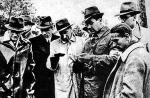 21 lub 22 maja 1943 roku. Józef Mackiewicz (w środku) w lesie katyńskim przegląda, wraz z delegatami robotników z Warszawy, dokumenty zamordowanych. Po jego lewej ręce dr Wodziński (z opaską PCK), z tyłu (w okularach) dziennikarz szwedzki muzeum katyńskie (repr. jerzy dudek)