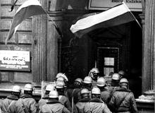 Milicjanci wchodzą  13 grudnia  1981 roku  do siedziby Zarządu Regionu „Solidarności” Ziemi Łódzkiej. Poszukujemy autora tego zdjęcia,  a także innych, niepublikowanych dotąd fotografii z okresu stanu wojennego. Zdjęcia te można obejrzeć na stronie  <a href=