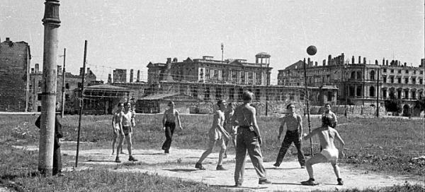 *1947 rok.  Rozgrywki siatkówki na pl. Zwycięstwa. W tle, po prawej, wypalony  gmach Hotelu Europejskiego. Mury trzymają się mocno